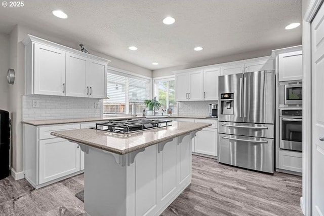 715 Shadowwood Loop, Keizer, OR 97303 - kitchen featuring appliances with stainless steel finishes, a textured ceiling, a breakfast bar, light wood-style floors, and white cabinets