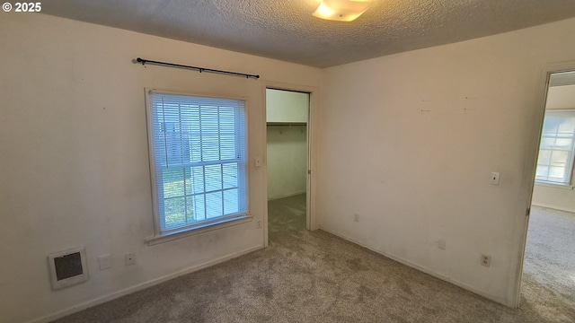 carpeted empty room featuring visible vents, a textured ceiling, and baseboards