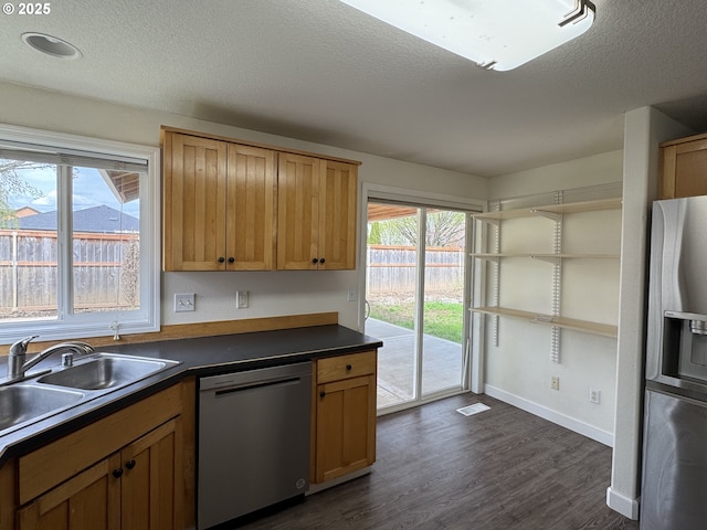 kitchen featuring a textured ceiling, dark countertops, dark wood finished floors, stainless steel appliances, and a sink