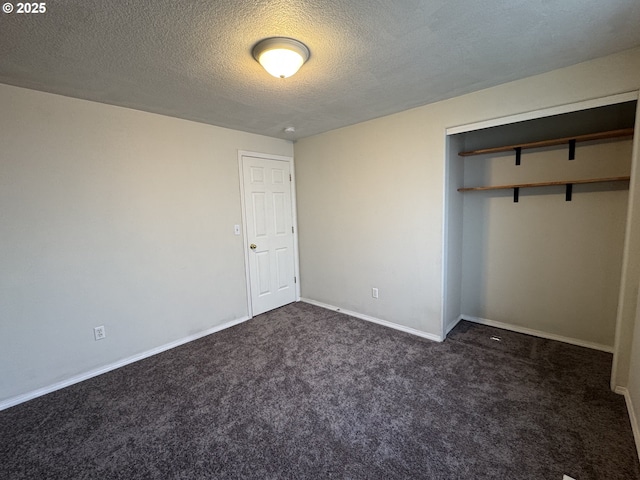 unfurnished bedroom with dark carpet, a textured ceiling, a closet, and baseboards