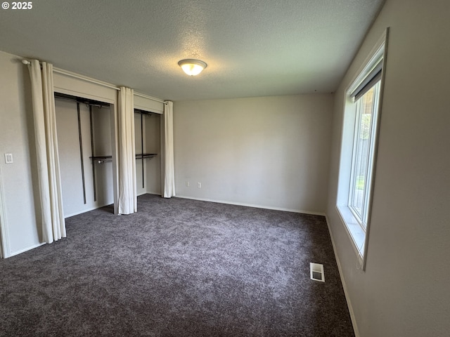 unfurnished bedroom featuring a textured ceiling, dark colored carpet, visible vents, and multiple closets