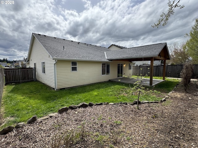 rear view of property featuring a shingled roof, a yard, a patio area, and a fenced backyard