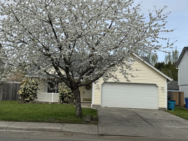 view of property hidden behind natural elements featuring driveway, a garage, fence, and a front yard