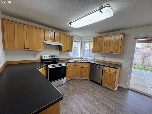 kitchen featuring a sink, appliances with stainless steel finishes, dark countertops, and under cabinet range hood