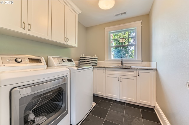 laundry room with washing machine and clothes dryer, cabinet space, a sink, dark tile patterned flooring, and visible vents