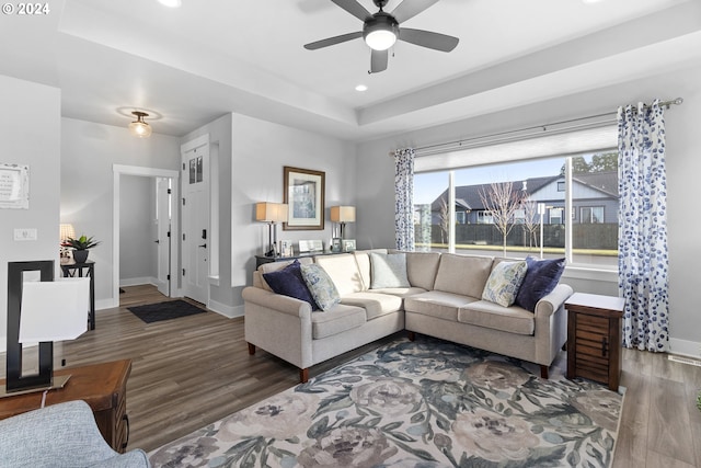 living room featuring dark hardwood / wood-style flooring, a raised ceiling, and ceiling fan