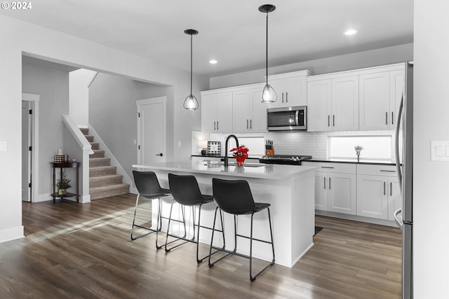 kitchen with backsplash, a kitchen island with sink, white cabinets, decorative light fixtures, and stainless steel appliances