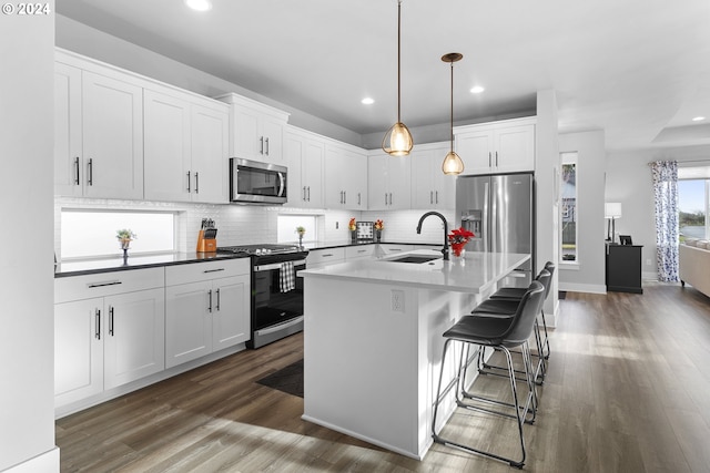 kitchen with appliances with stainless steel finishes, a kitchen breakfast bar, sink, white cabinetry, and an island with sink