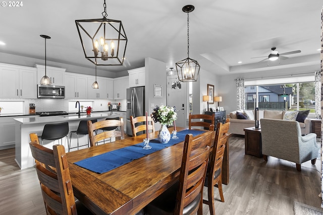 dining room featuring a tray ceiling, sink, dark hardwood / wood-style floors, and ceiling fan with notable chandelier