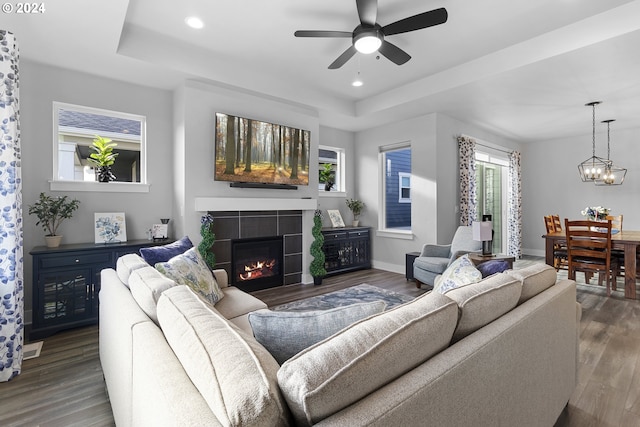 living room featuring ceiling fan with notable chandelier, dark hardwood / wood-style floors, a raised ceiling, and a tiled fireplace