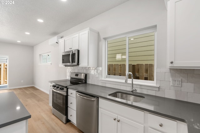 kitchen with sink, white cabinets, light wood-type flooring, a wall unit AC, and appliances with stainless steel finishes