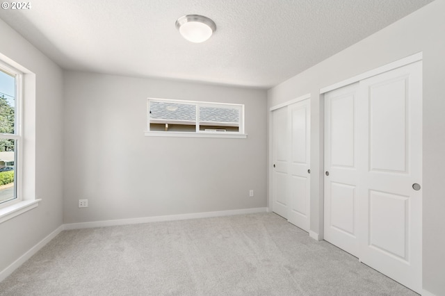 unfurnished bedroom featuring light carpet, multiple windows, and a textured ceiling