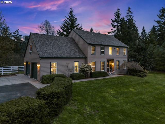 colonial inspired home with aphalt driveway, fence, a lawn, and roof with shingles