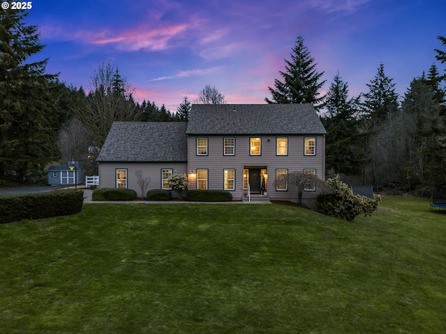 colonial inspired home featuring a front yard, a trampoline, and roof with shingles