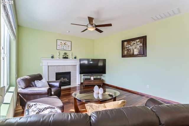 living area with a tiled fireplace, ceiling fan, wood finished floors, and baseboards