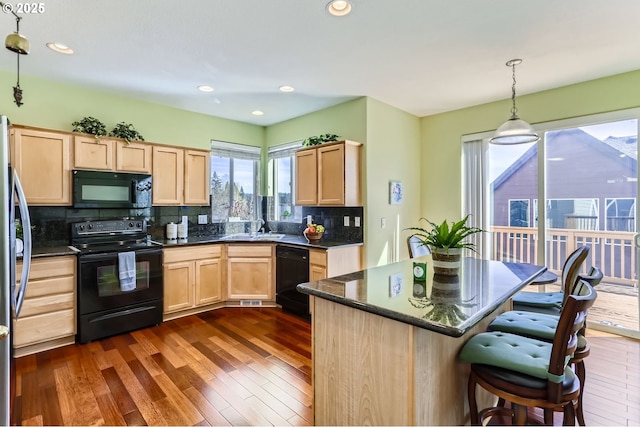 kitchen with black appliances, light brown cabinets, tasteful backsplash, a kitchen bar, and dark wood finished floors