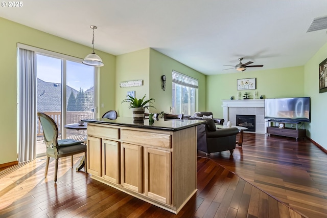 kitchen featuring dark countertops, a ceiling fan, dark wood-style floors, a fireplace, and a kitchen island