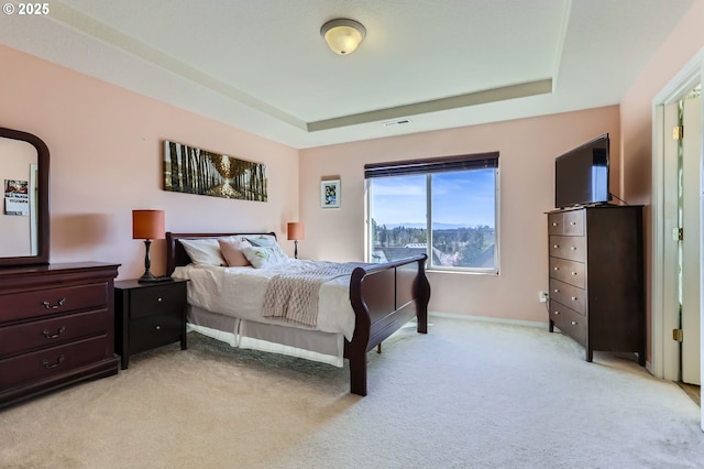 bedroom with a raised ceiling, light colored carpet, and baseboards