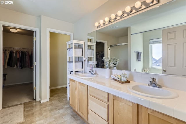 full bathroom with double vanity, a stall shower, a spacious closet, and baseboards