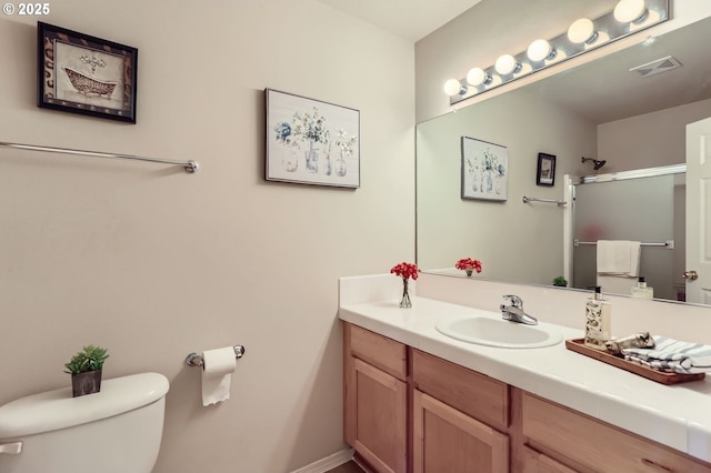 bathroom with toilet, vanity, a shower with shower door, and baseboards