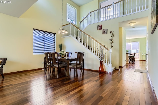 dining area featuring a towering ceiling, stairway, dark wood-style flooring, and baseboards