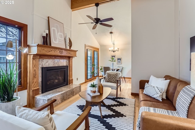 living room with a high end fireplace, wood-type flooring, beamed ceiling, high vaulted ceiling, and ceiling fan with notable chandelier