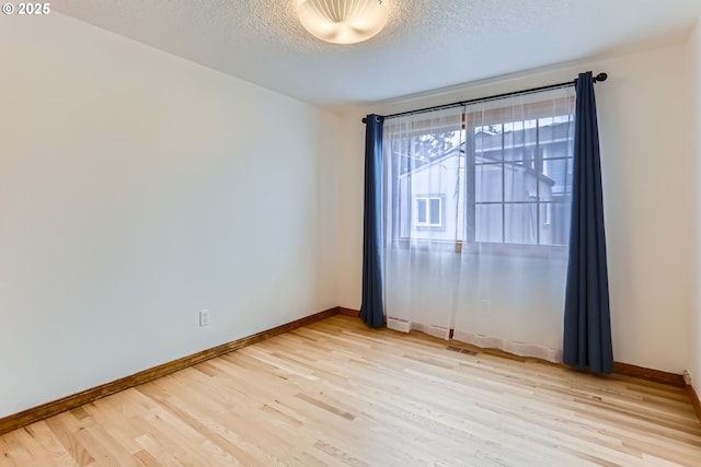 empty room with light wood-type flooring and a textured ceiling