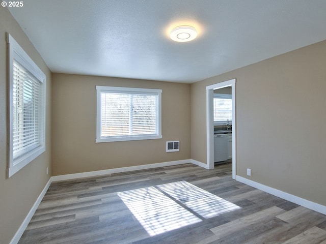 empty room with a sink, wood finished floors, visible vents, and baseboards