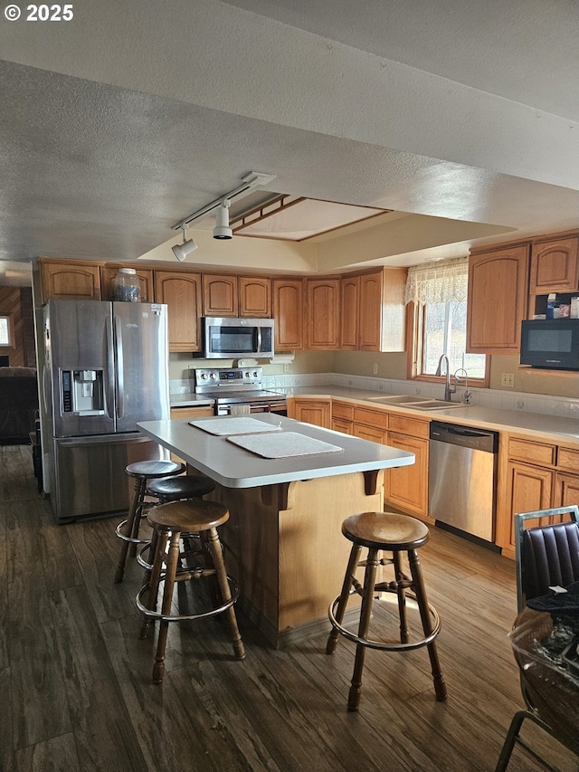 kitchen with appliances with stainless steel finishes, sink, hardwood / wood-style flooring, a center island, and a breakfast bar area