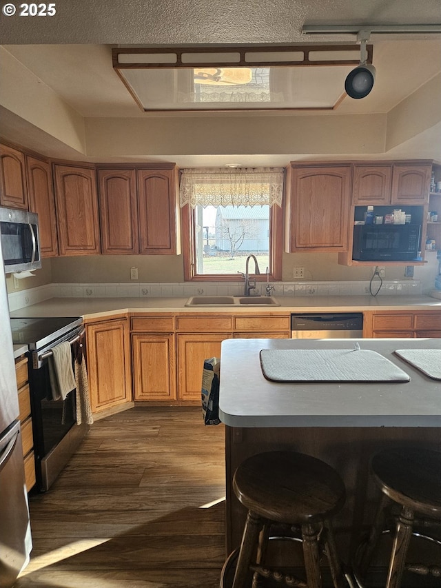 kitchen with a breakfast bar, track lighting, sink, dark hardwood / wood-style flooring, and stainless steel appliances