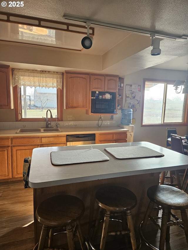 kitchen with track lighting, a wealth of natural light, sink, dishwasher, and a breakfast bar area