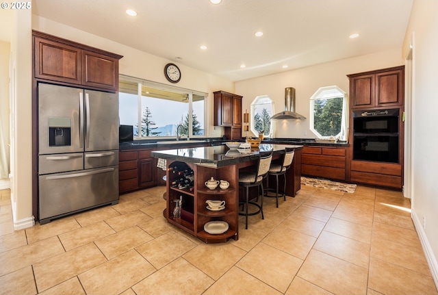 kitchen with wall chimney exhaust hood, a breakfast bar area, stainless steel fridge, double oven, and a kitchen island