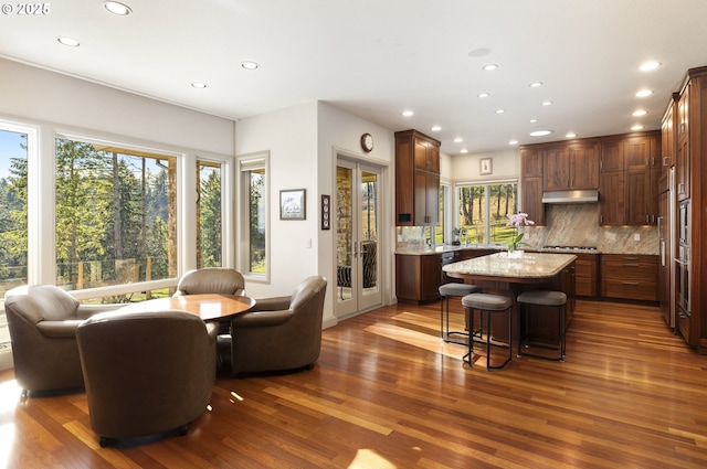 kitchen with light stone countertops, a kitchen bar, a kitchen island, backsplash, and dark hardwood / wood-style flooring