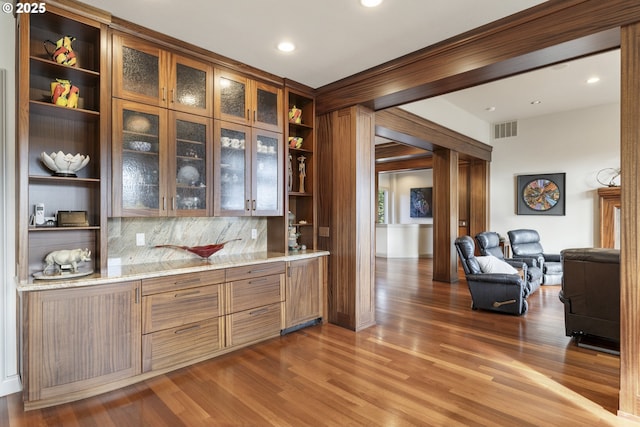 bar with decorative backsplash, light stone counters, and dark wood-type flooring