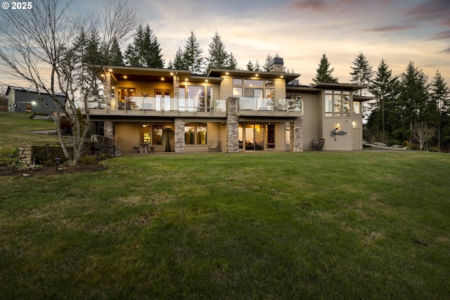 back house at dusk with a yard and a balcony