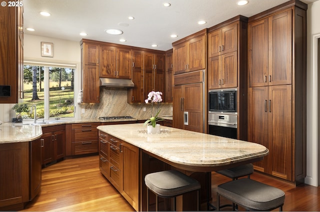 kitchen with light wood-type flooring, built in appliances, light stone countertops, a breakfast bar, and decorative backsplash