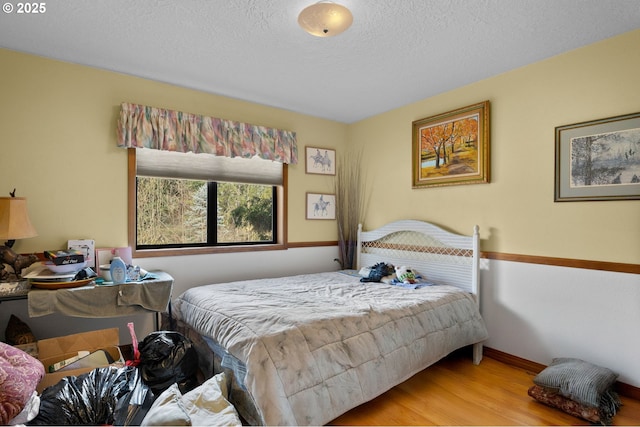 bedroom featuring a textured ceiling, baseboards, and wood finished floors