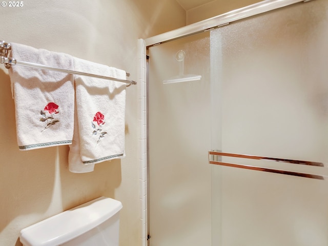 bathroom featuring a shower with door and toilet