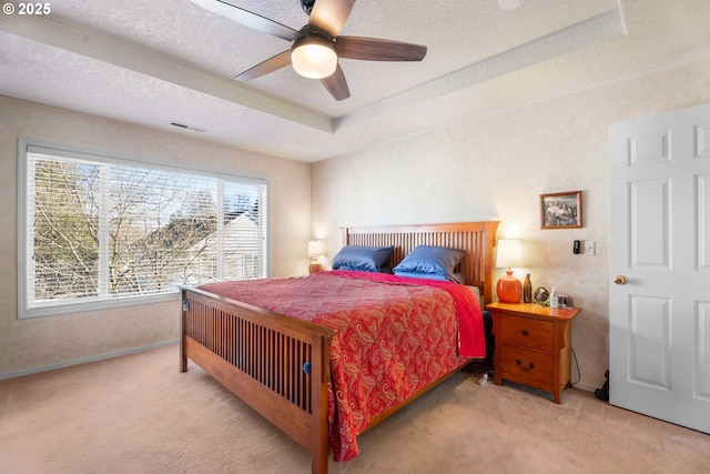 bedroom featuring a tray ceiling, ceiling fan, light carpet, and a textured ceiling