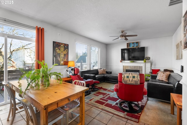 living room featuring a tile fireplace, light tile patterned floors, a textured ceiling, and ceiling fan