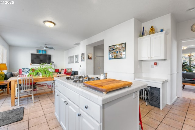 kitchen with breakfast area, ceiling fan, light tile patterned floors, tile counters, and white cabinetry