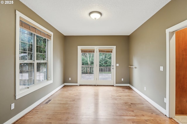 interior space with a textured ceiling, visible vents, light wood-style flooring, and baseboards