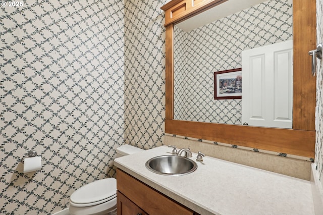 half bath featuring vanity, toilet, and wallpapered walls