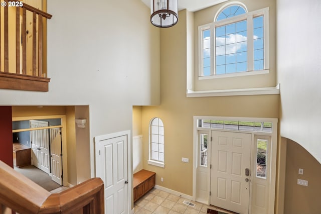 foyer featuring a towering ceiling, light tile patterned floors, baseboards, and visible vents