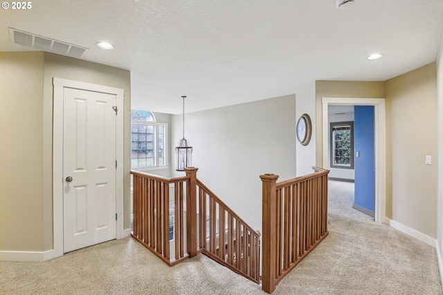 corridor with carpet flooring, an upstairs landing, visible vents, and baseboards