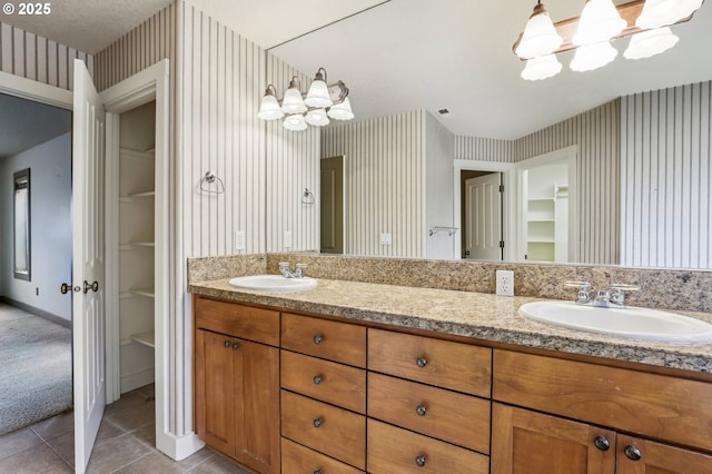 full bath with tile patterned flooring, wallpapered walls, a sink, double vanity, and an inviting chandelier