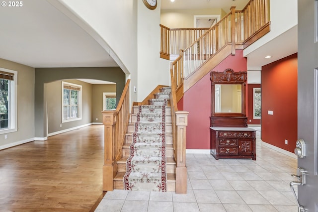 stairs featuring a towering ceiling, baseboards, arched walkways, and wood finished floors