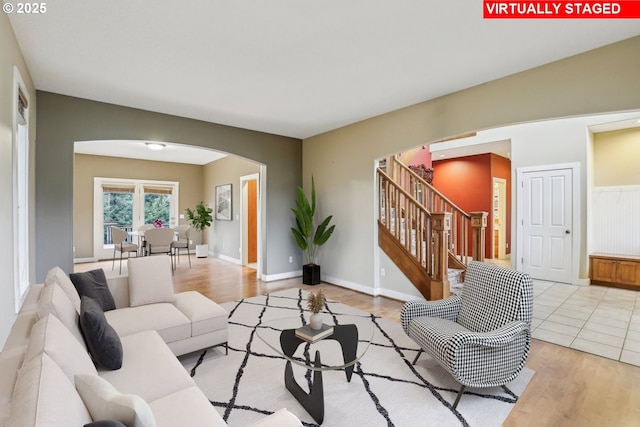 living room with light wood finished floors, baseboards, stairs, and arched walkways