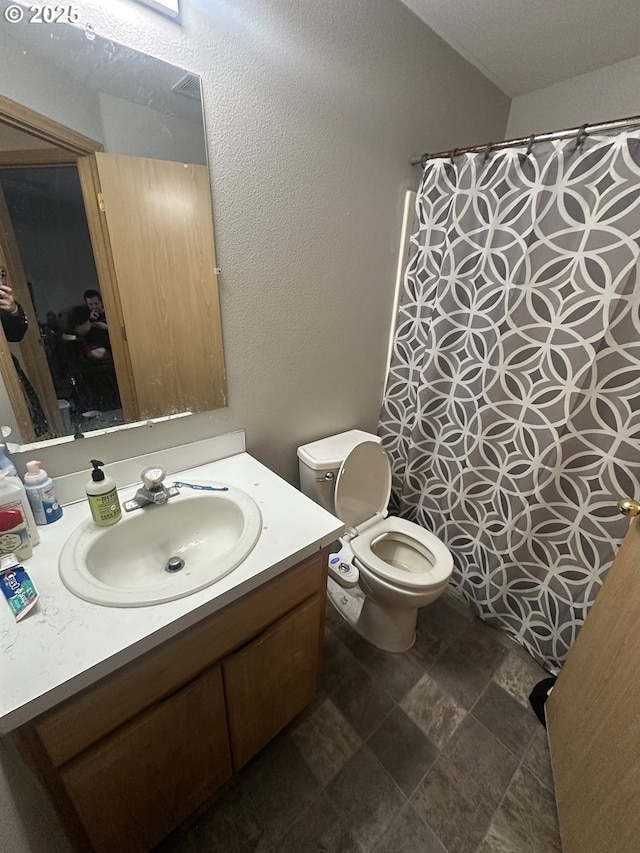 full bathroom featuring toilet, curtained shower, a textured wall, and vanity