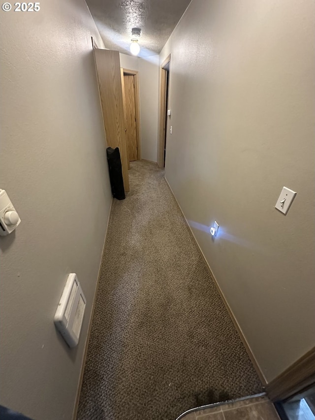 hallway with a textured ceiling, carpet, and baseboards